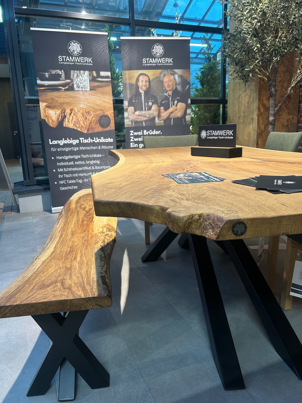 Esstisch aus Eiche mit Naturkante auf einem Sterngestell im Showroom, dahinter Aufsteller von STAMWERK
