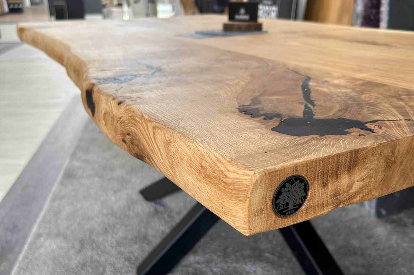 Esstisch aus Eiche mit Naturkante auf einem X-Gestell aus Stahl, an der Stirnseite das Emblem des TableTags