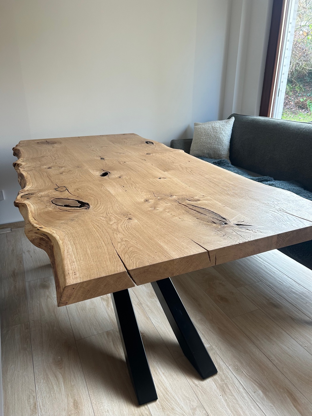 Esstisch aus Eiche mit Naturkante in einem Wohnraum, dahinter ein graues Sofa